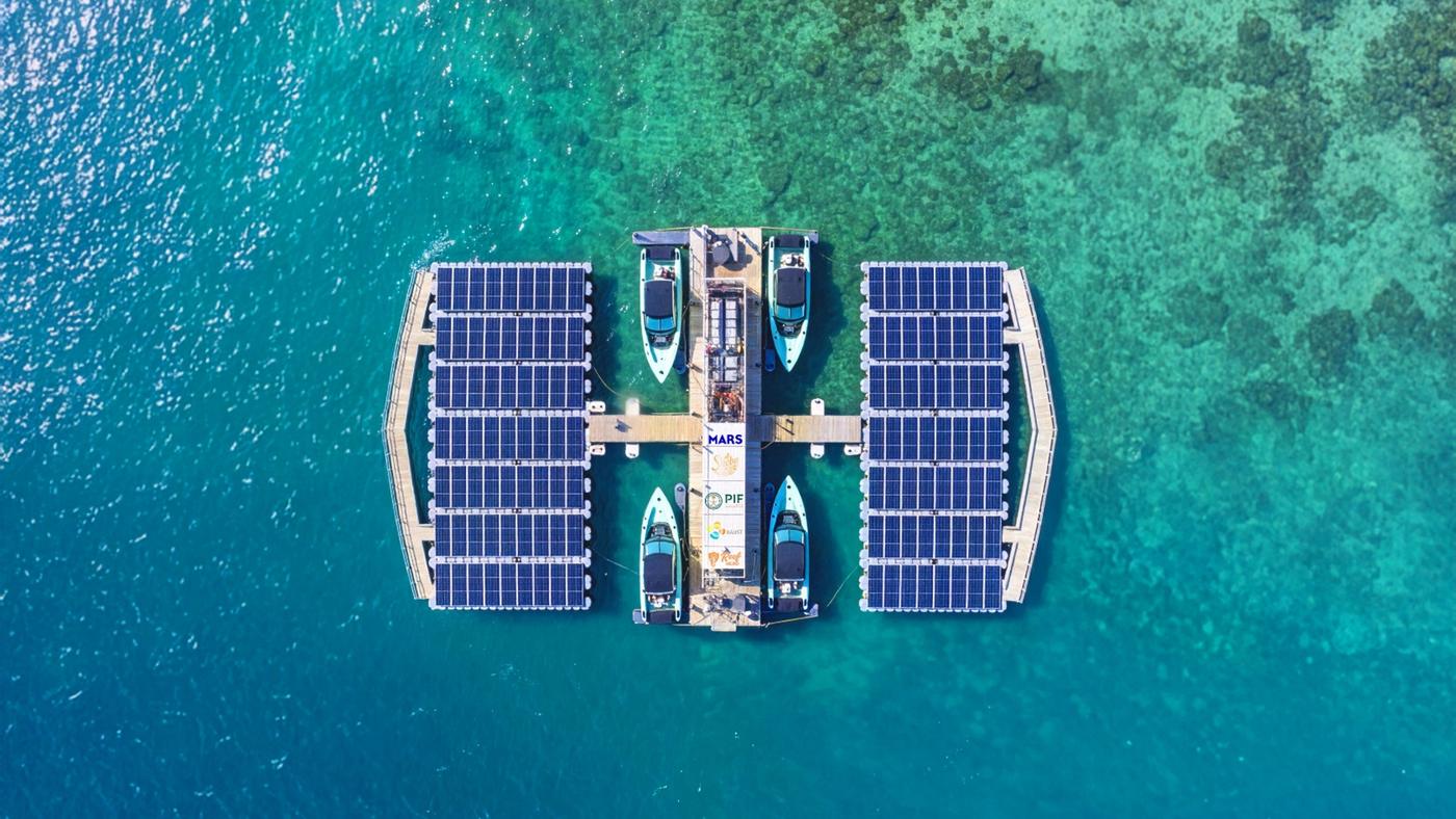 A ReefHealer platform seen from directly overhead, solar arrays along both arms and four boats moored to it